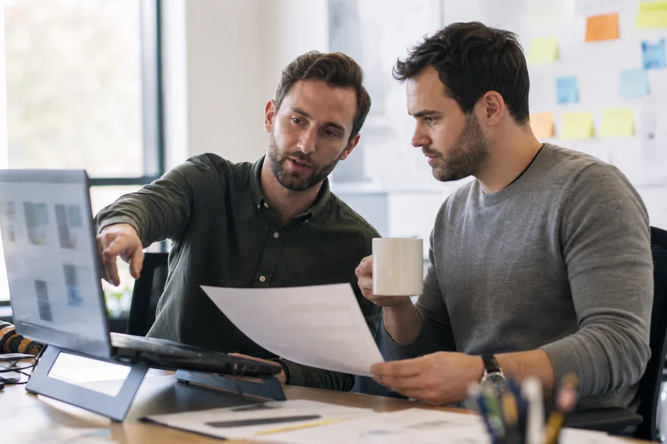 Two agency account managers reviewing client workspaces on a laptop
